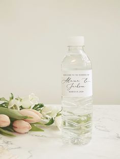 a bottle of water sitting on top of a table next to some pink and white flowers