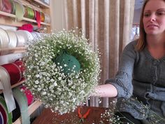 a woman sitting at a table with some flowers and thread spools in front of her