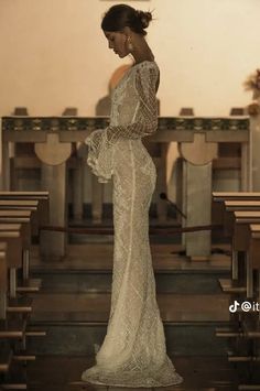 a woman standing in front of pews wearing a white dress and holding her hands on her hips