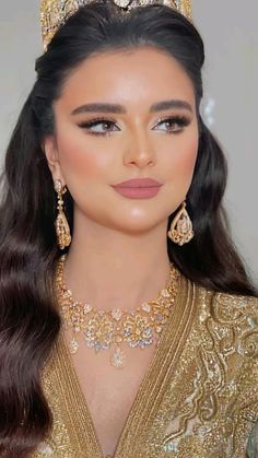 a woman with long hair wearing a gold dress and tiara, looking at the camera