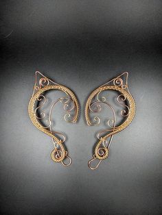 Just the right touch to spice up your fantasy costume. Add these beautiful ear cuffs to your elf costume for your next Ren Faire or use them as a fun bit of jewelry at your next D&D event. Golden Brass and Copper curls with intricate woven wire with a clear finish make these lovely ear cuffs a must have for your next fantasy event.  These ear cuffs have been polished to a bright shine and sealed with a clear coat. No piercings are necessary for these elf ears to stay in place, the back wire rides behind the ear similar to a pair of glasses and the front decorations provide gentle pressure to keep the cuffs in place. Each cuff is approximately 4 inches in height and 2 inches in width. Handmade Adjustable Cartilage Earrings For Party, Handmade Adjustable Fantasy Ear Cuff, Fantasy Style Festival Ear Cuff For Pierced Ears, Whimsical Adjustable Ear Cuff For Festivals, Handmade Fantasy Body Jewelry For Party, Fantasy Style Festival Ear Cuff, Adjustable Wire Wrapped Fantasy Earrings, Handmade Fantasy Wrap Earrings, Adjustable Fantasy Wrap Earrings As Gift