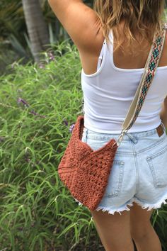 a woman in shorts and a white tank top is holding a brown crocheted purse