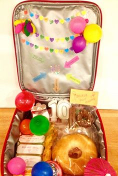 an open suitcase filled with lots of food and confetti on top of a wooden floor