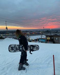 a person holding a snowboard on top of a snow covered slope in the evening