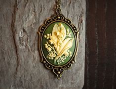 A beautiful cream colored cameo with detailed lily of the valley flowers and a green background set in antiqued brass paired with a long antiqued brass chain.  Details: Pendant measures approx 2.5 inches (6.35cm)  Necklace measures 24 inches (55.88cm) Chain and setting are plated brass Cameo is hard, matte resin Please allow for possible slight color differences due to different settings on different screens. Want a shorter chain? Just leave a note to seller at checkout for me and I can adjust i Victorian Green Cameo Jewelry, Antique Green Cameo Jewelry, Marine City, Green Lily, Lily Of The Valley Flowers, Valley Flowers, Cameo Jewelry, Necklace Green, Cameo Necklace