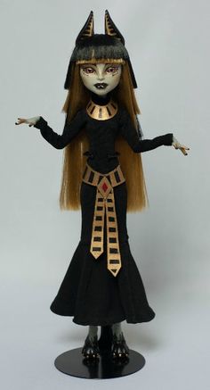 a doll dressed in black and gold with long hair wearing an egyptian headdress