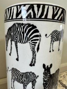 a white and black vase with zebras painted on the side, sitting on a marble countertop