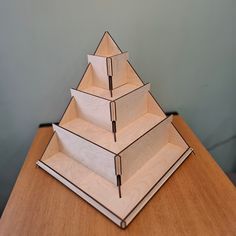 three pyramids made out of plywood sit on top of a wooden table in front of a gray wall