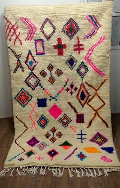 a white rug with multicolored designs and fringes on the floor next to a wall