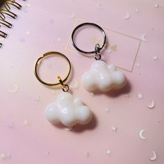 two white clouds are hanging from gold hoop earrings on a pink surface with stars and crescents