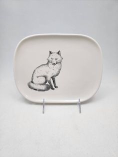 a white plate with a black and white fox design on the front, sitting in front of a gray background