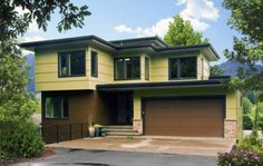 a two story house with green siding and brown garage doors on the front door is surrounded by greenery