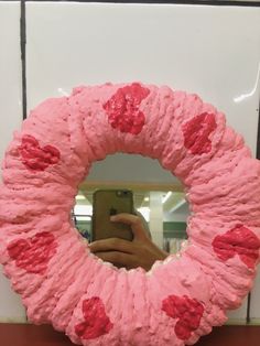 a person taking a photo of a pink wreath made out of toilet paper with hearts on it