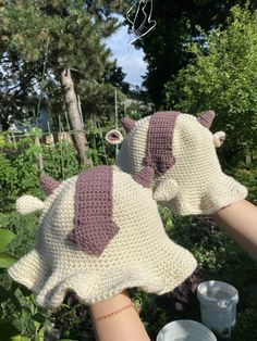 two crocheted cow mitts are held in the air by someone's hand