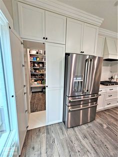 a stainless steel refrigerator and freezer combo in a kitchen with white cabinets, wood flooring