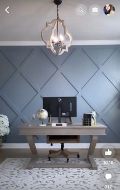 a desk with a computer on it in front of a blue wall and chandelier