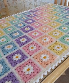 a crocheted blanket with flowers on it sitting on top of a wooden table