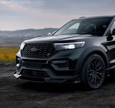 the front end of a black suv parked on a dirt road with mountains in the background