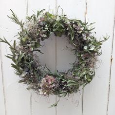 a wreath hanging on the side of a white door with flowers and plants in it