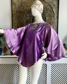 💜 Beautiful vintage late 1960s to early 1970s purple slippery satin tunic top.  Features wide angel sleeves, A-line shape, rounded front and back bottom hem, boat neckline finished with purple velvet. Handmade to a very good standard 💜 💜 There is a very faint area of colour variation on the front but it's so faint you really have to look hard to see it. This does not detract from the beauty of this garment though 💜  💜Fits sizes XS-Small. Best for bust up to 34 inches (18 inches across seam to seam). Length approximately 30 inches shoulder to longest point at hem 💜  Bust: best for up to 34 inches Length: 30 inches approx. shoulder to bottom hem ANY ACCESSORIES SHOWN IN THE PHOTOS ARE NOT INCLUDED IN THE SALE UNLESS OTHERWISE STATED. ♡ Facebook: https://www.facebook.com/VicAndBertieVin Purple Silk Evening Top, Purple Satin Top For Spring, Spring Purple Satin Top, Purple Silk Party Tops, Purple Satin Party Top, Purple Bohemian Party Tops, Purple Bohemian Top For Party, Vintage Fitted Bell Sleeve Tops, Satin Tunic