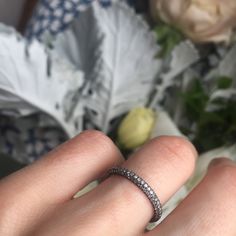 a woman's hand with a wedding ring on it and flowers in the background