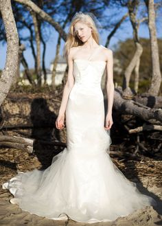 a woman in a white wedding dress standing on the sand with trees in the background