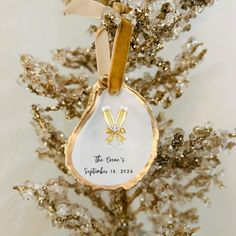 a gold and white ornament hanging from a christmas tree with a ribbon around it