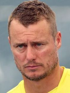 a close up of a person wearing a yellow shirt and looking at the camera with a serious look on his face