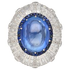 GIA Certified 26.47 Carat No Heat Sri Lanka Origin Blue Sapphire and Diamond Dome Art Deco Style Ring in 18K White Gold. Item Details: - Item Type: Cocktail Ring - Metal: 18 Karat White Gold - Weight: 14.13 Grams - Size: 6 Center Stone Details: - Type: Sapphire - Shape: Cabochon / Oval - Cutting Style: Double Cabochon - Transparency: Transparent - Color: Blue - Carat: 26.47 - Setting: Prong - Origin: Sri Lanka - Treatment: None - Measurements: 17.52 x 14.08 x 10.90 mm Side Stone Details: - 40 Ro Dome Art, Blue Star Sapphire Ring, Shades Of Dark Blue, Star Sapphire Ring, Blue Star Sapphire, Gold Cocktail Ring, Gold Cocktail, Blue Sapphire Diamond, Diamond Cocktail Rings