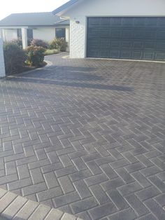 a brick driveway in front of a house with two garage doors on the other side