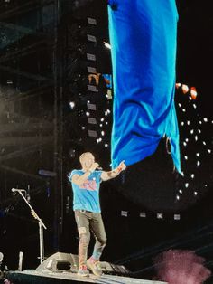 a man standing on top of a stage next to a giant blue piece of cloth