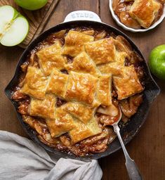 an apple pie in a cast iron skillet on a wooden table next to apples