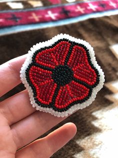 a hand holding a red and black beaded brooch