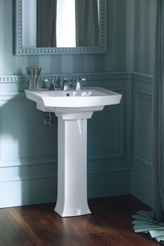 a white pedestal sink sitting under a mirror in a bathroom next to a wooden floor