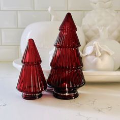 two red glass christmas trees sitting on top of a white counter next to a plate