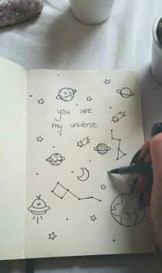 someone is writing on a notebook with space drawings