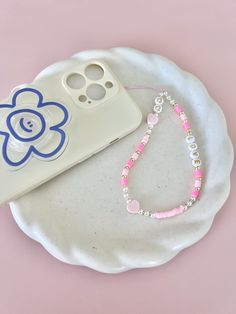 a pink beaded necklace sitting on top of a white plate next to a cell phone