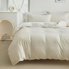 a large white bed sitting in a bedroom next to a fire place and a window