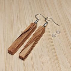 two wooden pieces of wood are hanging from silver earwires on a wooden surface