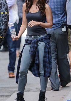 a woman in tight jeans and black boots is holding a water bottle while standing on the sidewalk