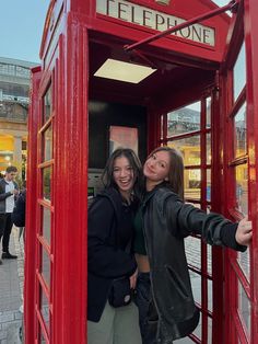 two women standing in a red phone booth