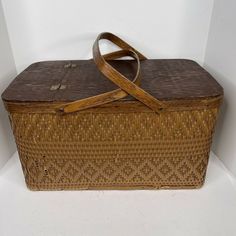 an old wicker basket with wooden handles and straps on the bottom, sitting against a white wall