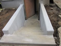 concrete steps leading up to an open door in a house under construction with dirt on the ground