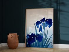 a vase sitting on the floor next to a painting with blue irises in it