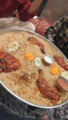 a large metal pan filled with food on top of a table next to other people