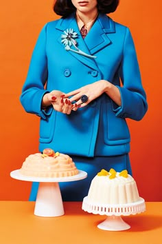 a woman in a blue suit standing next to two cakes