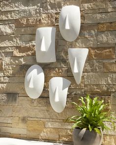 three white vases are hanging on a brick wall next to a potted plant