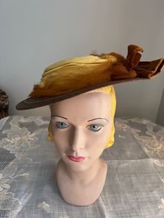 Antique brown  braided straw hat. It has a small round crown and small brim.  Around the crown is a yellow cotton  cloth and rust netting band. On one side is a brown velvet bow. The hat is an oval shape or more egg shape with the fro t being wider.At the back underneath is 2 green and brown silk flower shapes with brown velvet ribbon connecting them.If hat is tipped to one side the rear flowers can be seen but if set straight, they would not be seen very well.  Inside is lined in black fabric and there is an elastic cord. Measurements Inside circumference is about 18 inches Front to back 12 inches Across 10.5 inches  Crown 1.5 inches high Brim is 3.5 inches in the front and about 2 inches in the back. Condition - good   Brown straw is good and yellow cloth band is good. Rust netting is to Vintage Brown Hat Bands For Country Events, Vintage Mini Hats With Curved Brim For Costume, Vintage Short Brim Top Hat For Costume, Brimmed Brown Hat For Vintage Events, Vintage Hats For Kentucky Derby And Country Events, Vintage Brimmed Mini Hats For Costume, Brown Brimmed Hat For Vintage Events, Victorian Adjustable Hat For Church, Victorian Costume Hat With Curved Brim