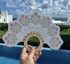 a person holding up a paper fan with flowers on it next to a swimming pool