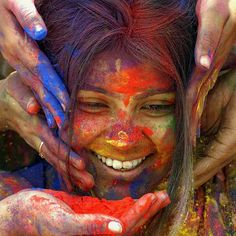 a woman is covered in colorful powder and holding her hands up to her face as she smiles